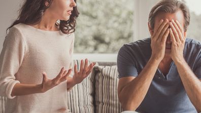 Couple of adults are quarreling while sitting on couch at home, man is covering his face