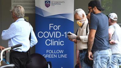 People wearing face masks walk past the sign for the COVID-19 Clinic at St Vincent's Hospital in Darlinghurst, Sydney. 