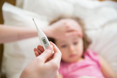 Close-up thermometer. Mother measuring temperature of her ill kid. Sick child with high fever laying in bed and mother holding thermometer. Hand on forehead.