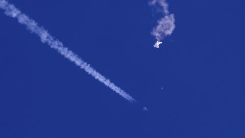 In this photo provided by Chad Fish, the remnants of a large balloon drift above the Atlantic Ocean, just off the coast of South Carolina, with a fighter jet and its contrail seen below it.