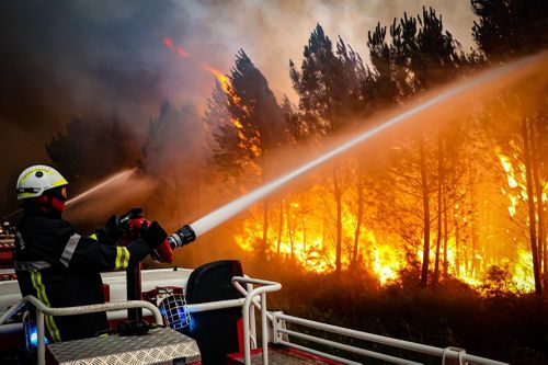 This photo taken on Friday July 15, 2022 by the fire brigade of the Gironde region (SDIS 33) shows firefighters using hose to fight a wildfire near Landiras, southwestern France, Thursday, July 14, 2022. 