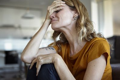 Woman with hands covering her face sitting on the floor at home