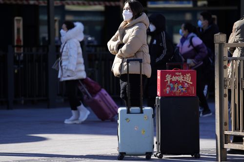 A traveller waits outside the Beijing Station with her trolley bags and a gift box with the words The taste of New Year in Beijing, China, Friday, Jan. 28, 2022. 