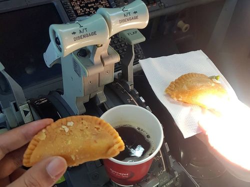 Two pilots drinking coffee and eating in their cockpit.