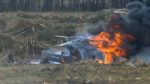 The co-pilot (left) stands next to the flaming wreckage of the Russian Mi28N helicopter. (Anton Nasonov/RZN.info)