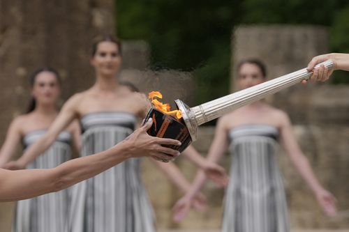 Actress Mary Mina, playing high priestess, right, lights a torch during the official ceremony of the flame lighting for the Paris Olympics