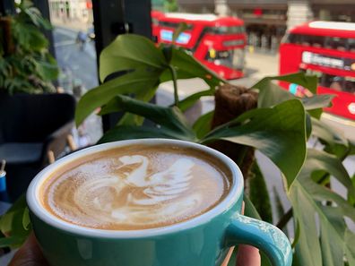 An oat milk latte decorated with a swan overlooks red buses and shops on London's Oxford Street