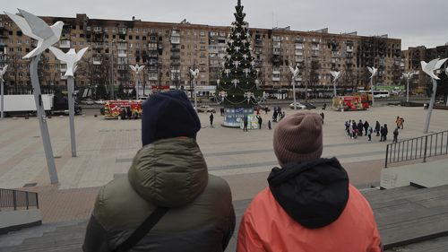 Local citizens walk near a Christmas tree decorated for Orthodox Christmas and the New Year festivities in Mariupol, in Russian-controlled Donetsk region, eastern Ukraine, Thursday, Jan. 5, 2023. (AP Photo/Alexei Alexandrov)