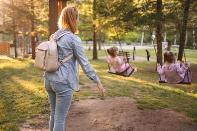 Mum and daughters at the playground, pushing daughters on a swing in the park.