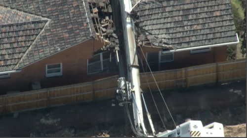 The fallen drill rig has caused significant damage to the roof of the home.