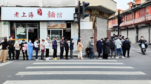 2022 年 3 月 11 日，星期五，上海一家医院的居民在街边一家面馆附近排队接受 COVID-19 检测。 