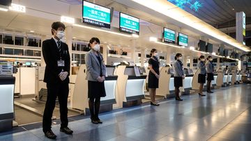 Ground staff stand in front of a check-in counter at Haneda airport in Tokyo, Japan.