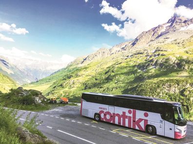 A Contiki-branded bus driving along a mountainous road.