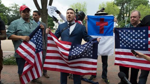 One year after the racially-stoked Charlottesville violence, a contingent of about 30 white nationalists is marching down a Washington street toward the White House surrounded by a protective bubble of police officers and vehicles.