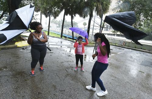 Umbrellas held by Janesse Brown, left, and her daughter Briana Johnson, 12, right, get torn apart by strong winds as Kyra Johnson, 8 watch, while they tried to visit Southbank Riverwalk in Jacksonville. (AP)