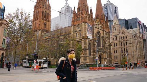 A woman walks past Melbourne's St Paul's Cathedral while wearing a face mask.