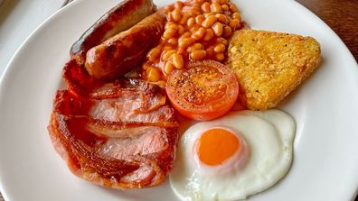Close up of a traditional full English breakfast with sausages, bacon, beans, grilled tomato, hash brown and fried egg.