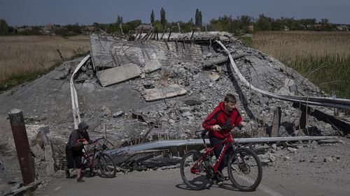Teenagers on bicycles pass a bridge destroyed by shelling near Orihiv, Ukraine