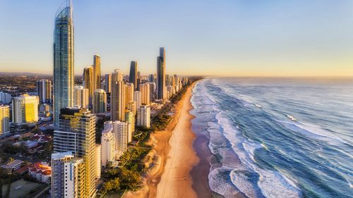 Waterfront behind sandy beach of SUrfers paradise greeting rising sun over Pacific ocean. Aerial view along Gold Coast and line of high-rise towers.