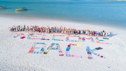 Whitsunday residents create giant beach towel sign to welcome back tourists