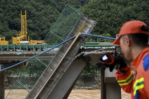 A rescuer looks at the collapsed bridge as they conduct a search and rescue on a river in Zhashui County in Shangluo City