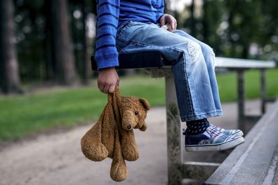 Young boy holding teddybear while alone on the bleachers