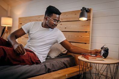 Young man wearing eyeglasses keeping wrist watch aside on side table while relaxing and calling it a day at night at home