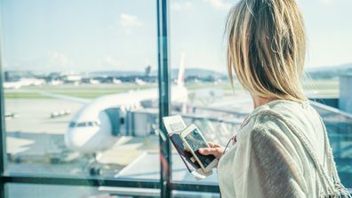 Young woman in airport waiting for flight sitting on bench with phone and passport in hands