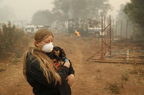 Arianne Harvey holds her dog T.J. near a truck still on fire from the Camp Fire in Paradise, California.