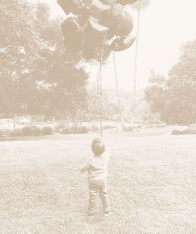 In the photo Archie is standing with his back to the camera holding a large bunch of balloons.