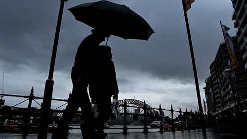 A man and child walk along Circular Quay shielding themselves from the rain with their umbrella. Sydney, NSW. 19th July, 2022. Photo: Kate Geraghty