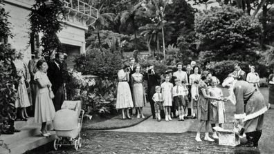 The Queen and Duke of Edinburgh stand on the steps of Government House, Auckland, New Zealand, on Christmas Day. Father Christmas gives presents to the Governor General's two young daughters. (Photo: 25 December, 1953)