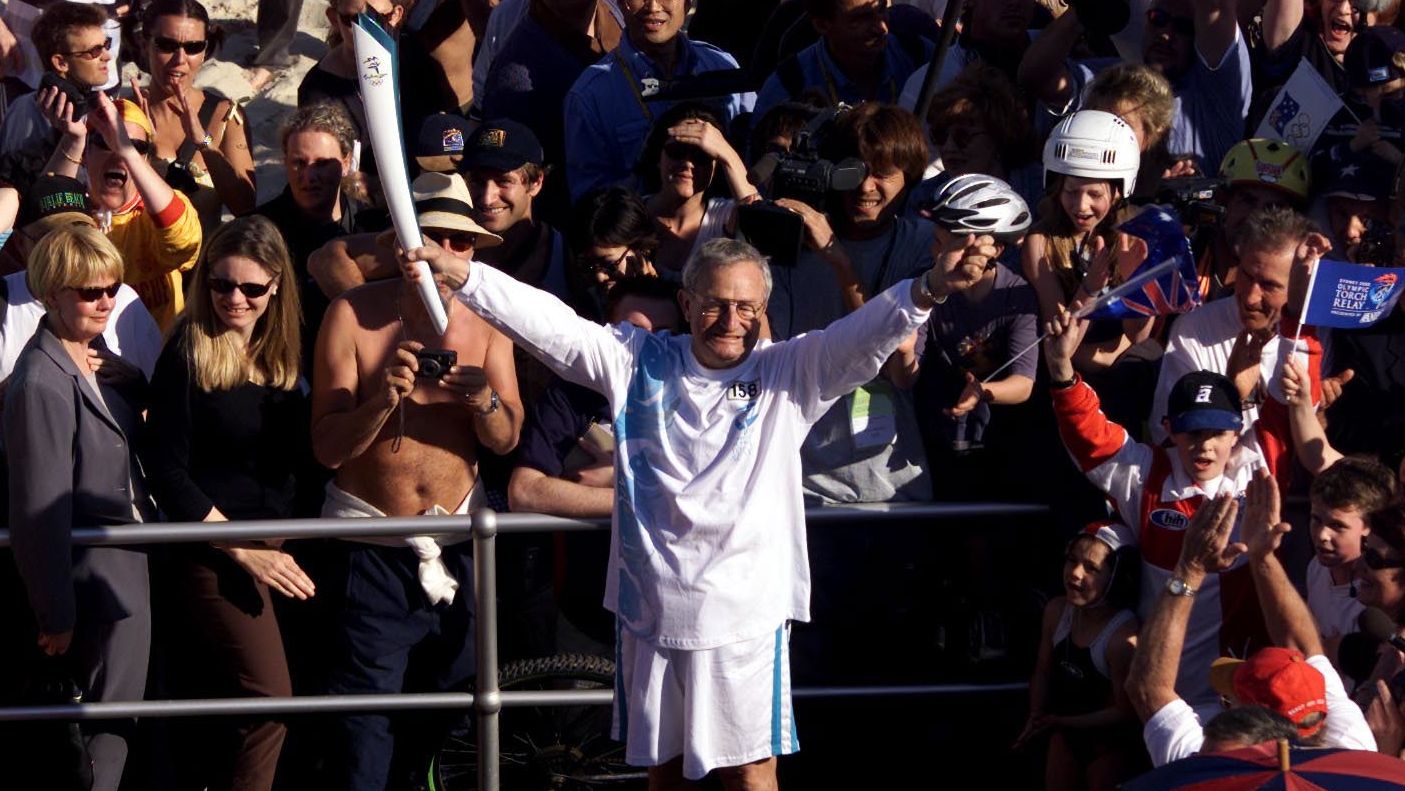 IOC delegate Phil Coles holds the Olympic torch aloft during the torch relay at Bondi Beach in preparation for the Sydney 2000 Olympic Games.