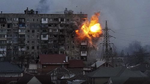 An explosion tears a hole in the side of an apartment building after a Russian tank fired a rocket in Mariupol, Ukraine.