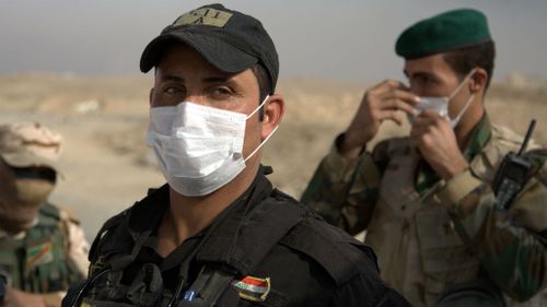Iraqi troops wear masks as they guard a checkpoint near the village of Awsaja, Iraq