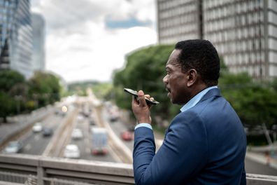 Mature businessman talking on mobile speaker phone while walking on the street