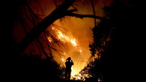 A firefighter takes a cell phone picture during a wildfire Saturday, Dec. 16, 2017, in Montecito, Calif. The so-called Thomas Fire is now the third-largest in California history. (AP Photo/Chris Carlson)