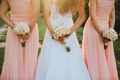 The bride and bridesmaids in an elegant dress is standing and holding hand bouquets of pastel pink flowers and greens with ribbon at nature. Young beautiful girls holds a wedding bouquet outdoors.