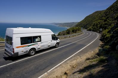 A campervan tours along a windy road through the hills and by the ocean. The day is a clear and blue, ideal for touring. This image has lots of copy and cropping space.