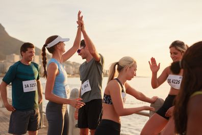 Runners giving high five to each other after a training session. Group of athletes celebrating success after a race.