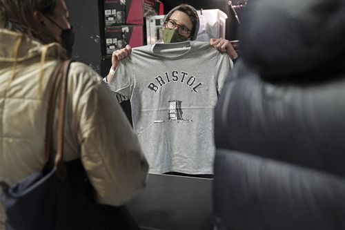 A person inside Rough Trade in Bristol, England, Saturday Dec. 11, 2021, holds up a T-shirt designed by street artist Banksy, being sold to support four people facing trial accused of criminal damage in relation to the toppling of a statue of slave trader Edward Colston. 