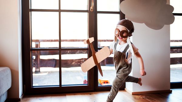 A toddler boy with carton plane and clouds playing indoors at home, flying concept.