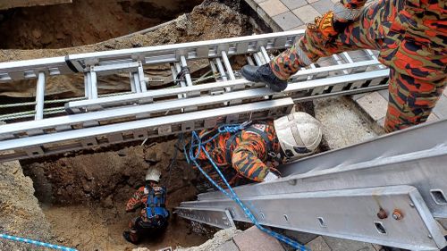 This photo provided by the Malaysia Fire and Rescue Department shows rescue personnel entering a deep sinkhole after receiving reports that a woman fell into the sinkhole after a section of the pavement collapsed in Kuala Lumpur, Friday, Aug. 23, 2024. 