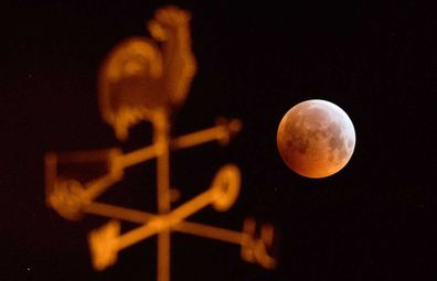 21 January 2019, Lower Saxony, Laatzen: Darkened, the full moon appears as a so-called "blood moon" and appears reddish - photographed behind a weathercock on the roof of a house. Moon, sun and earth are exactly in one line during a lunar eclipse.