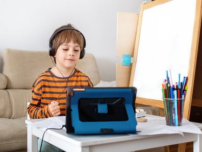 Happy little boy attending online classes from home. Child using digital tablet and headsets for connecting with teacher and schoolmates. School education and social distance during quarantine