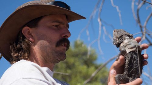 Dr Kristoffer Wild holding a bearded dragon in southwest Queensland.