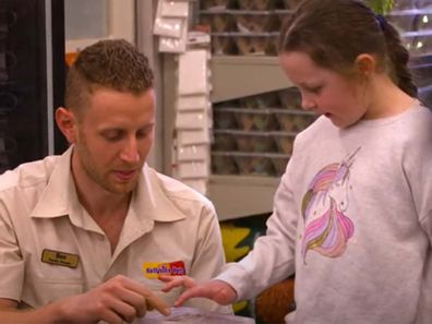 Man kneeling, showing a standing girl on the right a box of bearded dragon eggs