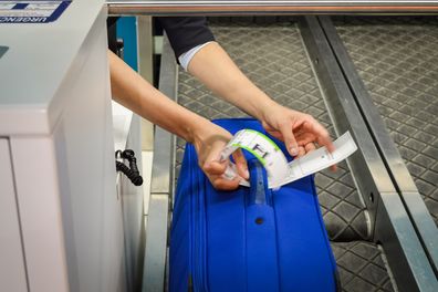 check-in employee attaches a luggage tag to suitcase of passenger - close up of hands