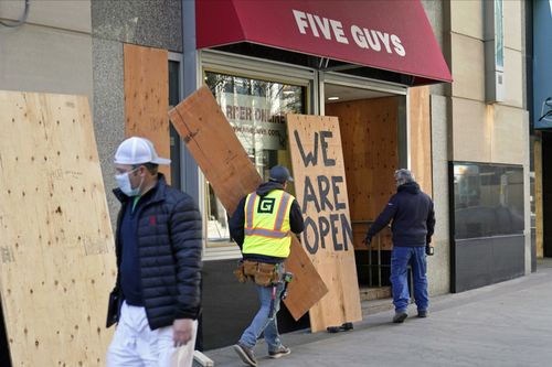 A passerby walks past workers boarding up a Five Guys restaurant along the Nicollet Mall Monday, Nov. 2, 2020, in Minneapolis ahead of the contentious presidential election on Tuesday. Many businesses along the popular downtown mall have been boarded up following unrest that followed the death of George Floyd at the hands of Minneapolis police on Memorial Day. (AP Photo/Jim Mone)