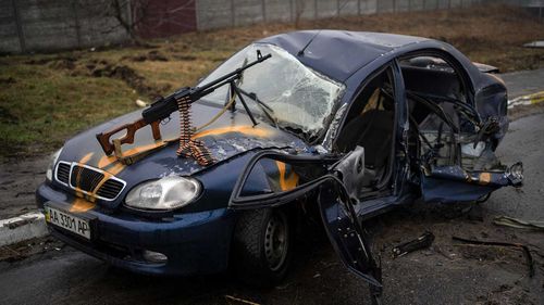 A machine gun propped on the bonnet of a totalled car in Ukraine.